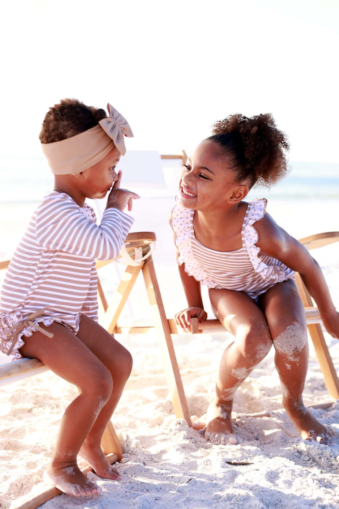 two sisters sitting on beach chairs wearing coordinating sandy stripes swimsuits 