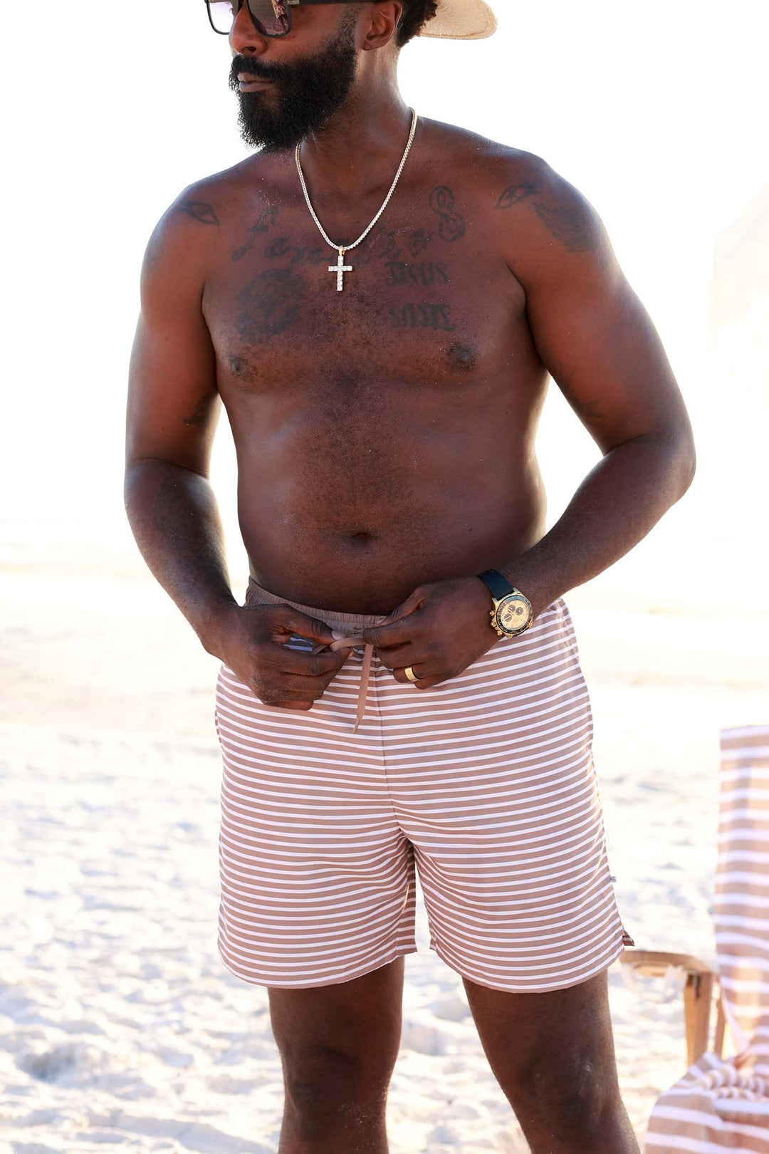 man standing on the beach tying swim trunks with brown neutral stripe print 
