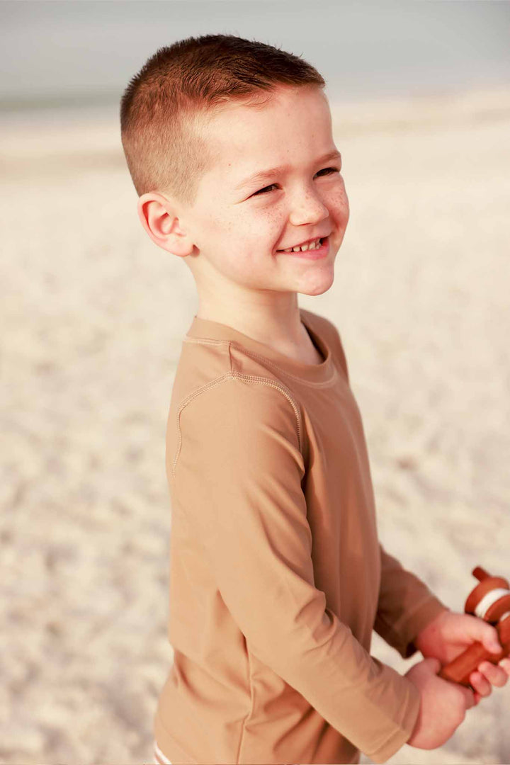 boy standing on beach fishing wearing a medium brown rash guard shirt 