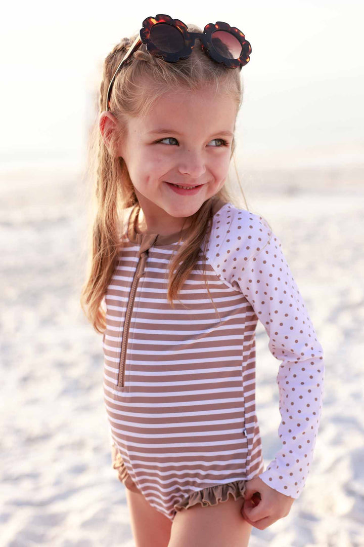 girl looking over her should with tortoise floral sunglasses on her head and a long sleeve stripe and polka dot front zip rash guard romper 