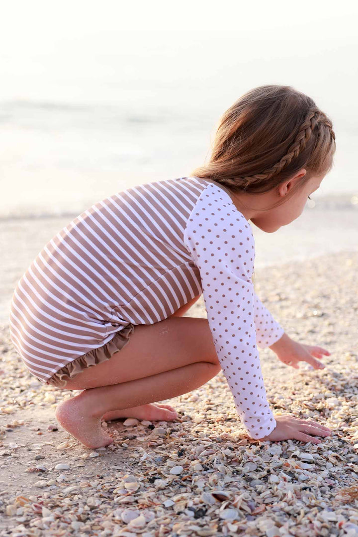 girl leaning down on beach wearing a stripe and polka dot neutral long sleeve rash guard 