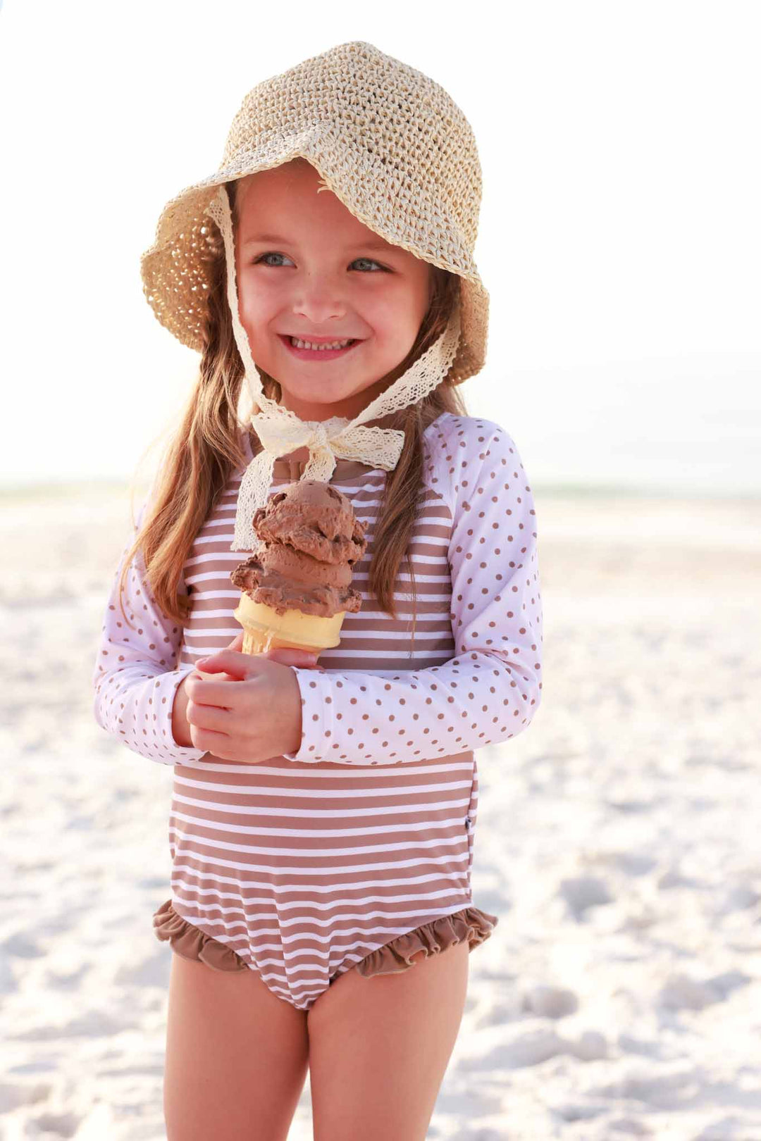 girl at the beach holding an ice cream cone wearing a brown and white stripe long sleeve rash guard swim romper with front zipper 