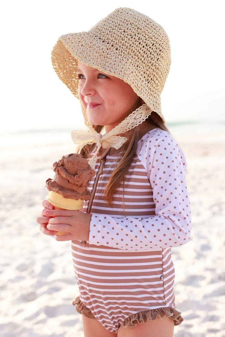 smiling girl at the beach in neutral stripe and dot swim romper holding an ice cream cone 