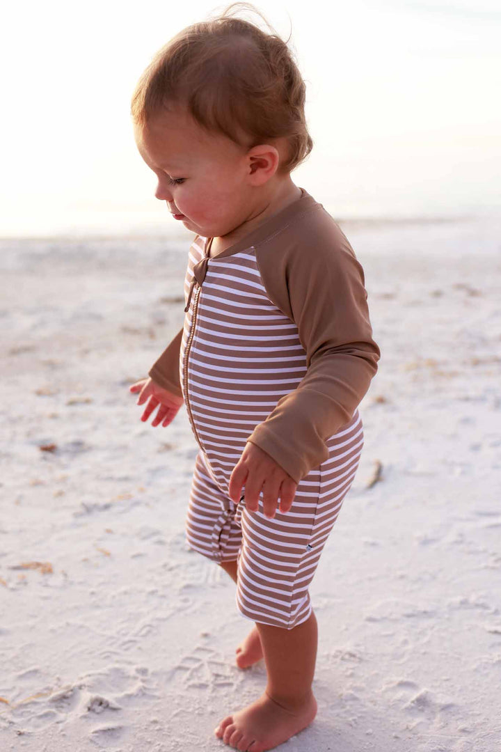 baby boy walking on beach wearing the sandy stripes long sleeve rash guard shortie romper 
