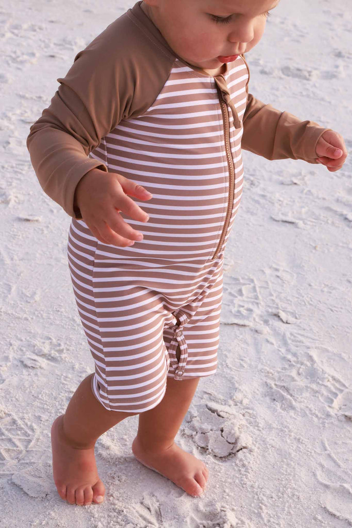 baby boy walking on the beach wearing the sandy stripes long sleeve rash guard shortie romper 