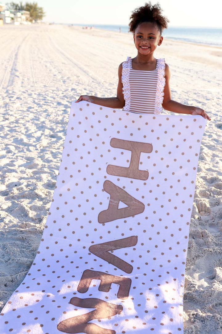 girl holding a white personalized beach towel with brown polka dots 