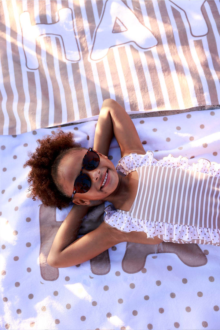 girl laying on personalized beach towel with brown polka dots with a brown stripe towel in the background 