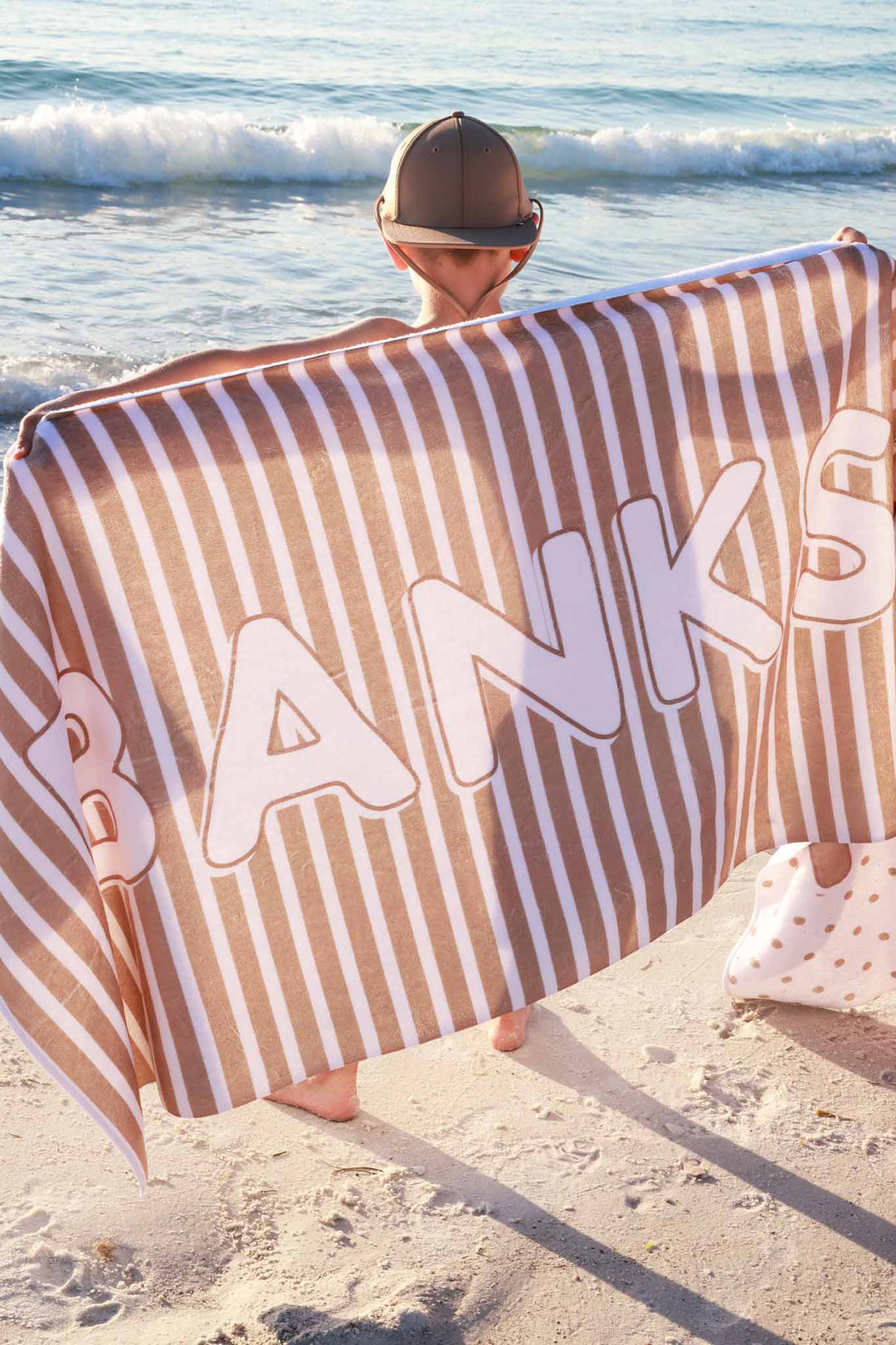 bow holding a brown stripe personalized beach towel behind his back wearing a matching hat 