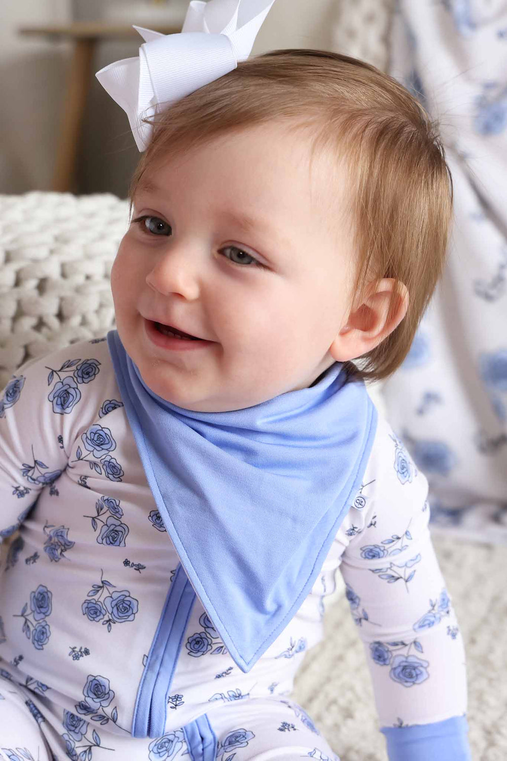 baby girl in blue rose convertible zip romper pajama with matching blue bandana bib and white clip bow