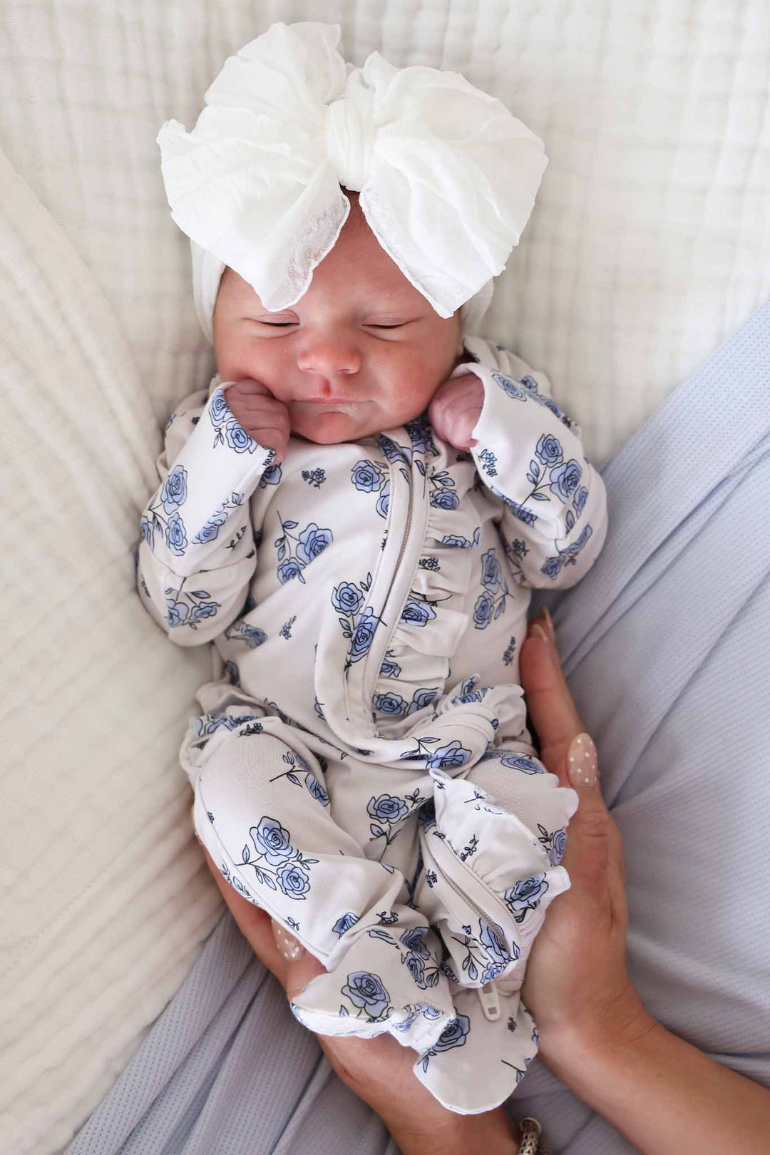 bunched up  newborn baby girl in sapphire garden ruffle zipper footie with ruffle knit bow on her head 