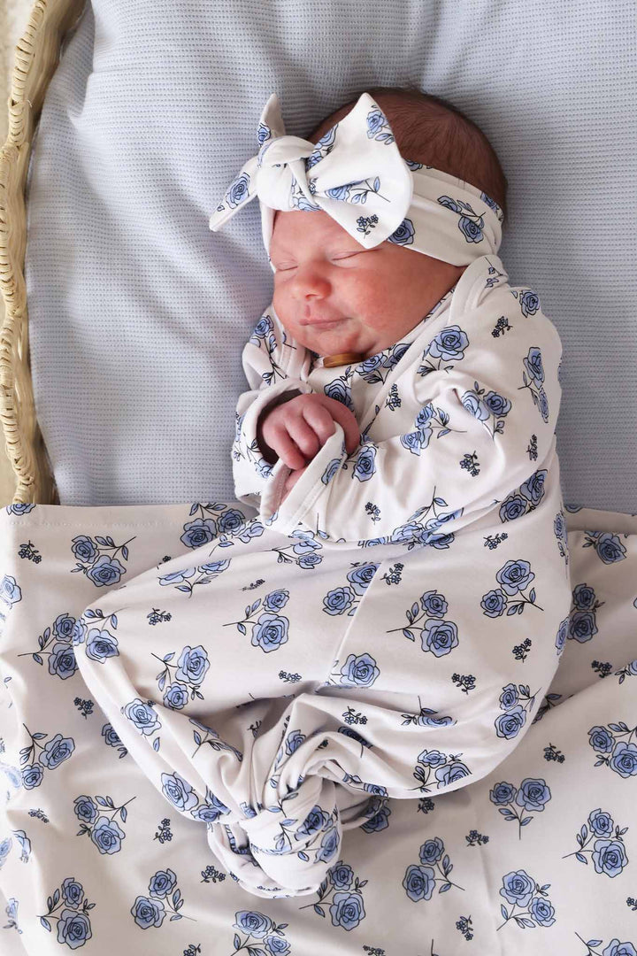 baby laying on side in basket in blue rose newborn knot gown with matching headwrap and swaddle blanket 