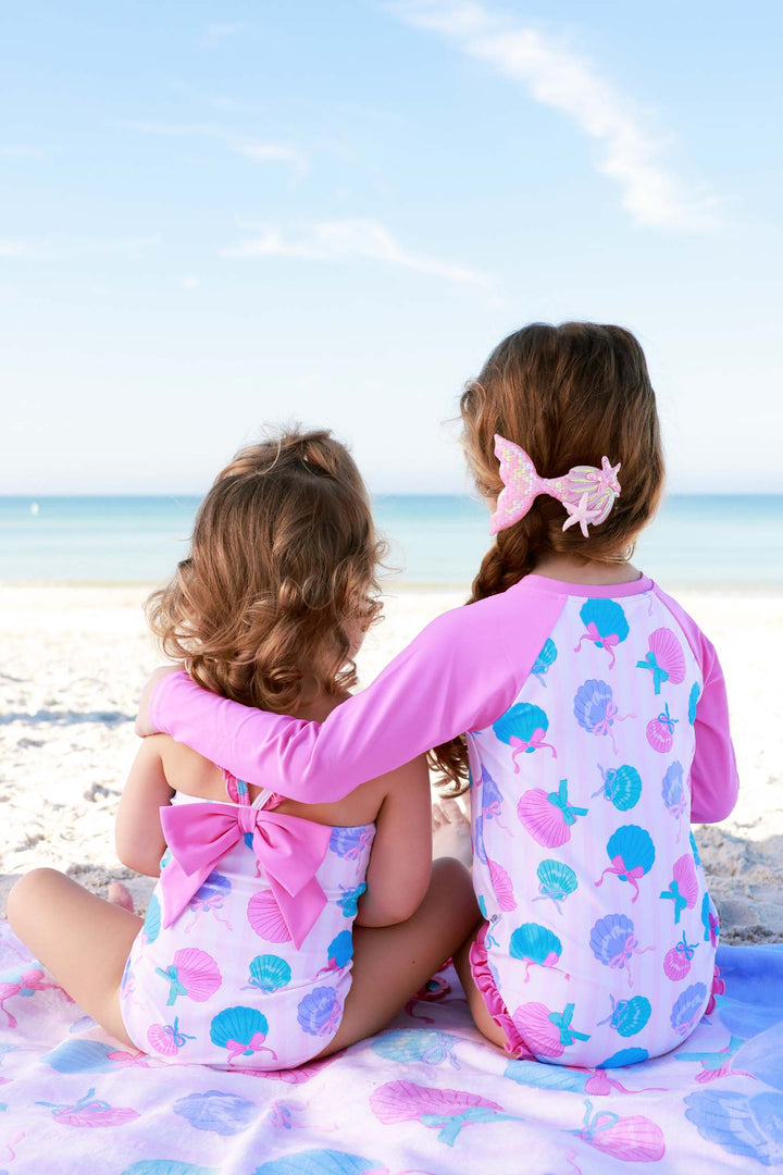 sisters sitting on the beach in seaside sweetie swimsuits 