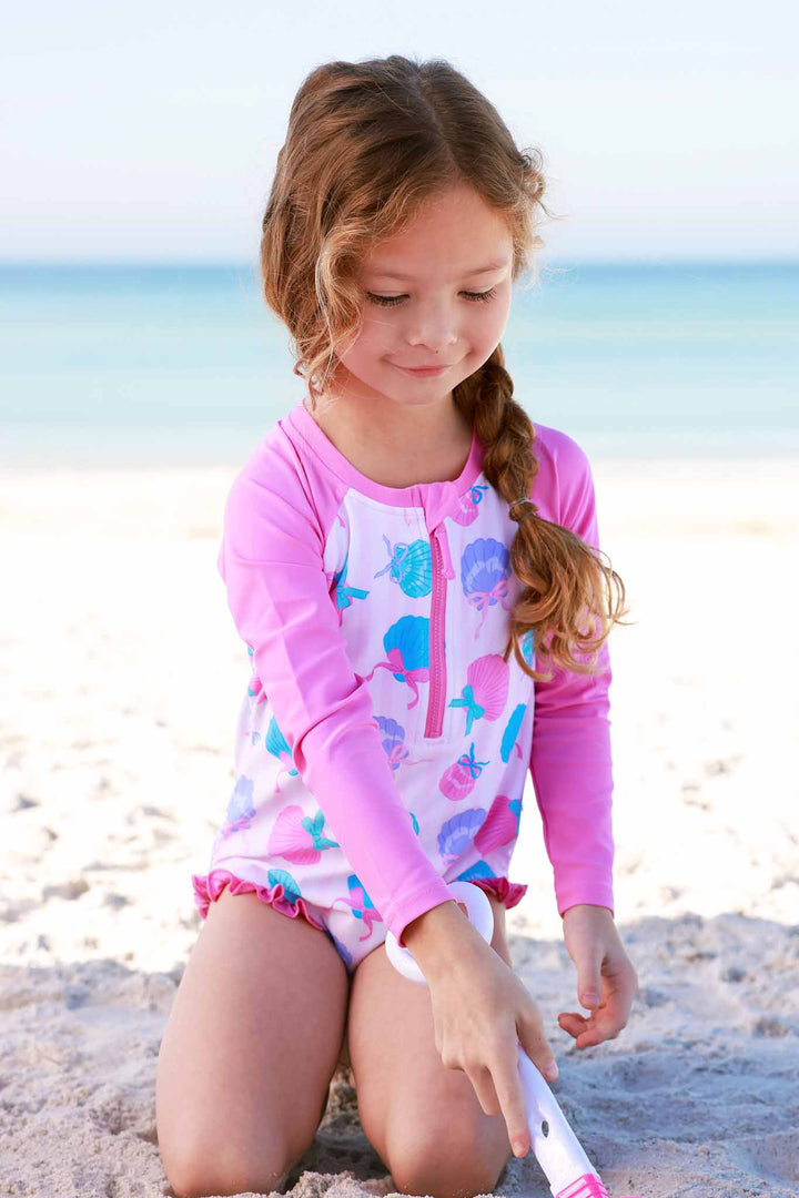 girl playing in sand in seashell front zip rash guard swimsuit 