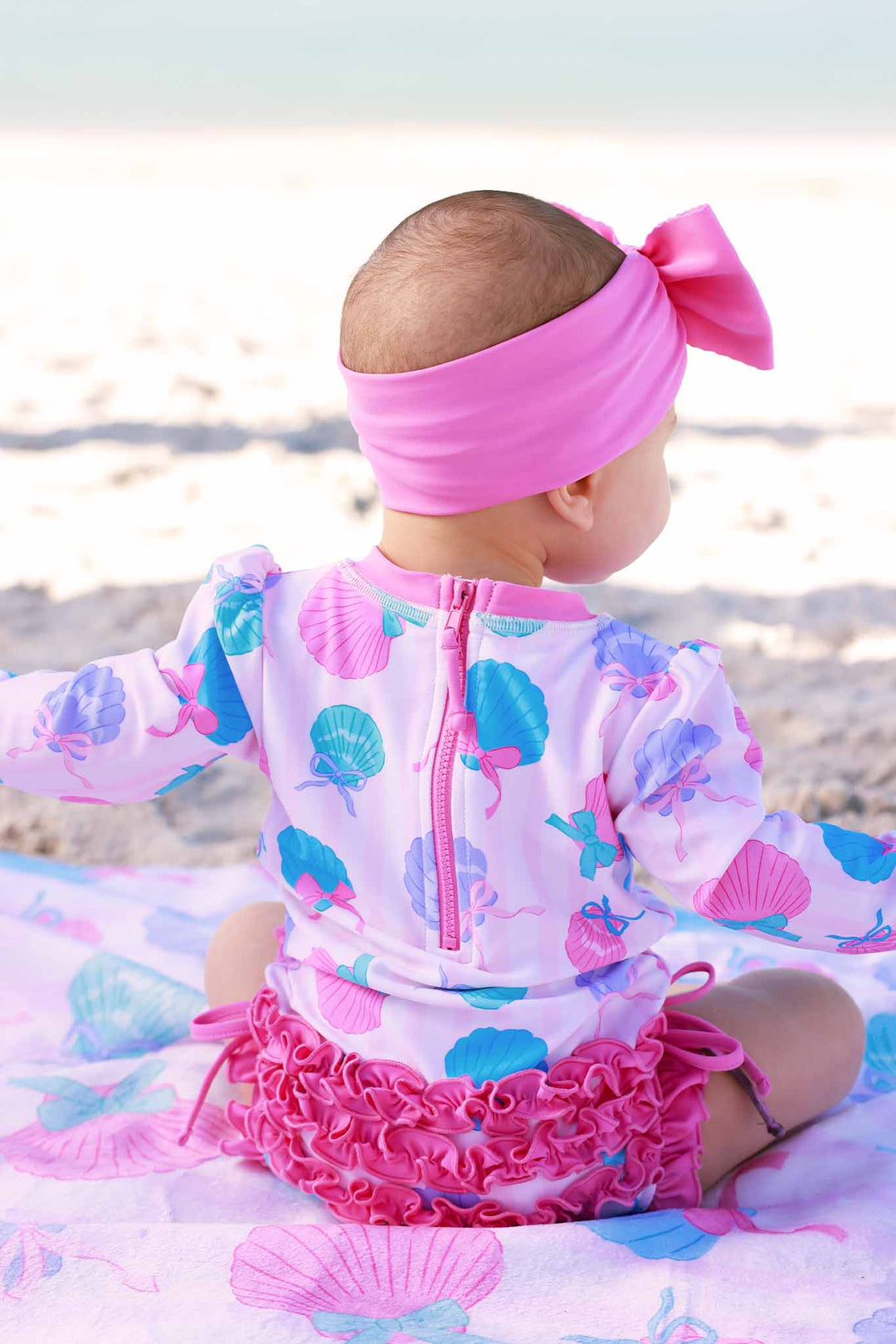 back view on seashell long sleeve rash guard with ruffle bottom with matching pink swim bow