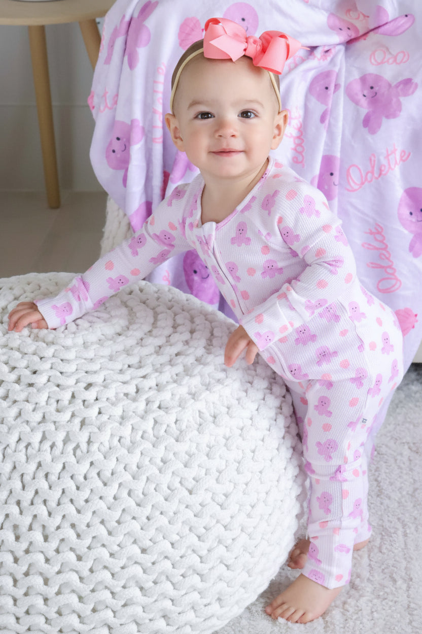 smiling baby in sea snuggles bamboo waffle convertible zip romper with coral bow headband — personalized sea snuggles kids blanket in background