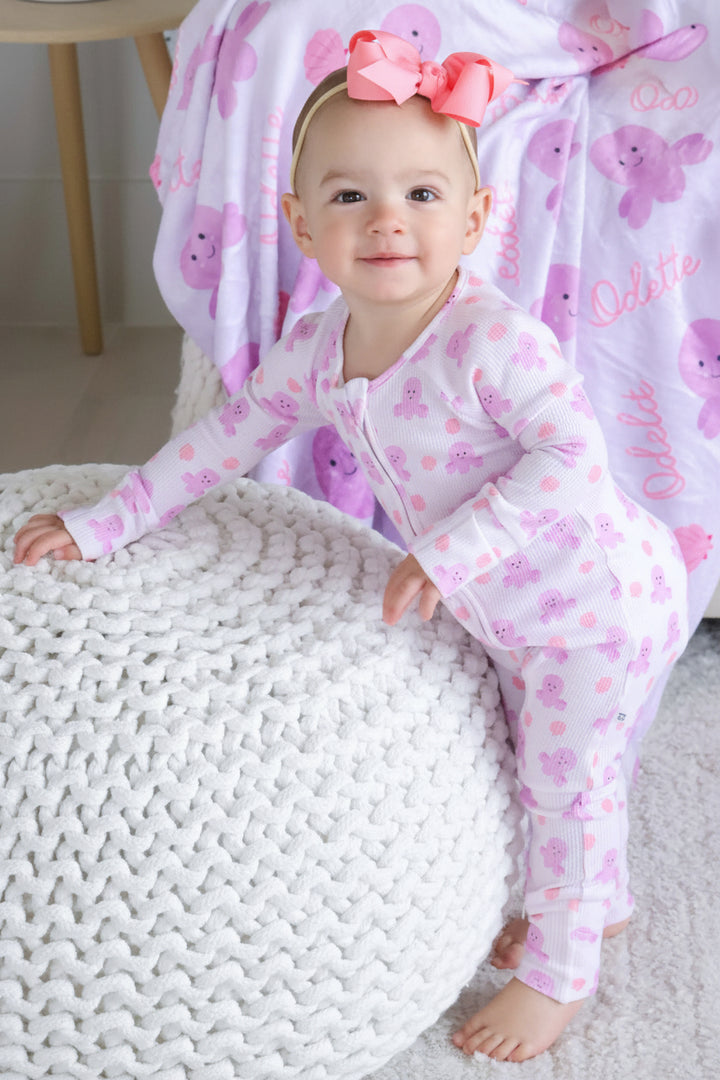 smiling baby in sea snuggles bamboo waffle convertible zip romper with coral bow headband — personalized sea snuggles kids blanket in background