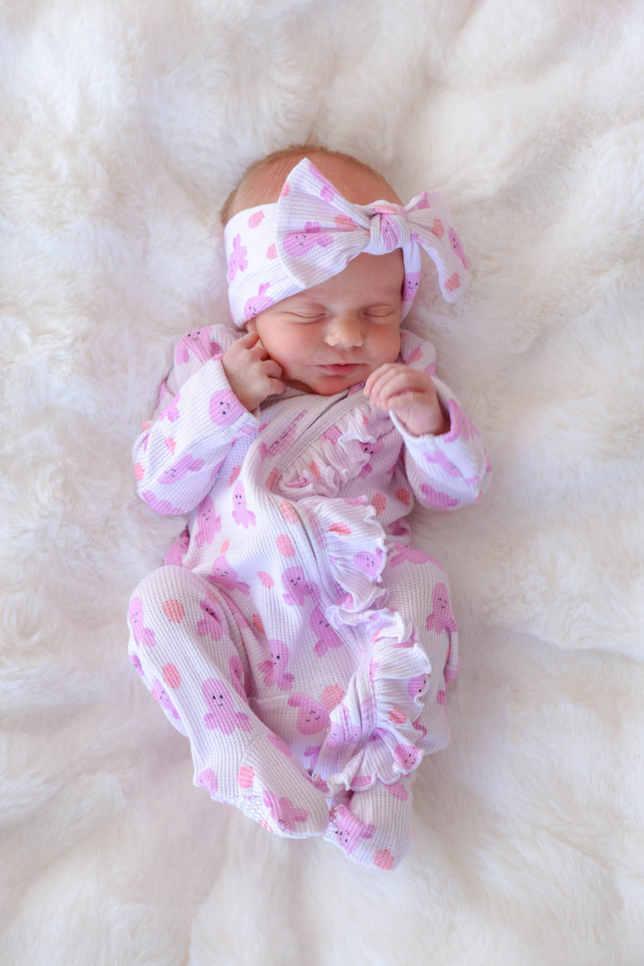 newborn in sea snuggles bamboo waffle ruffle zipper footie with matching bamboo waffle knit bow headwrap on white fur