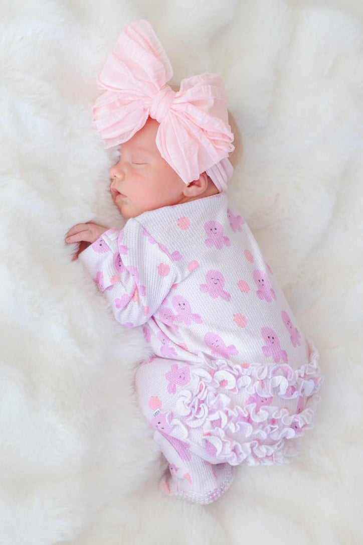 newborn sleeping on white fur in sea snuggles bamboo waffle ruffle zipper footie — back view with pink bow headband