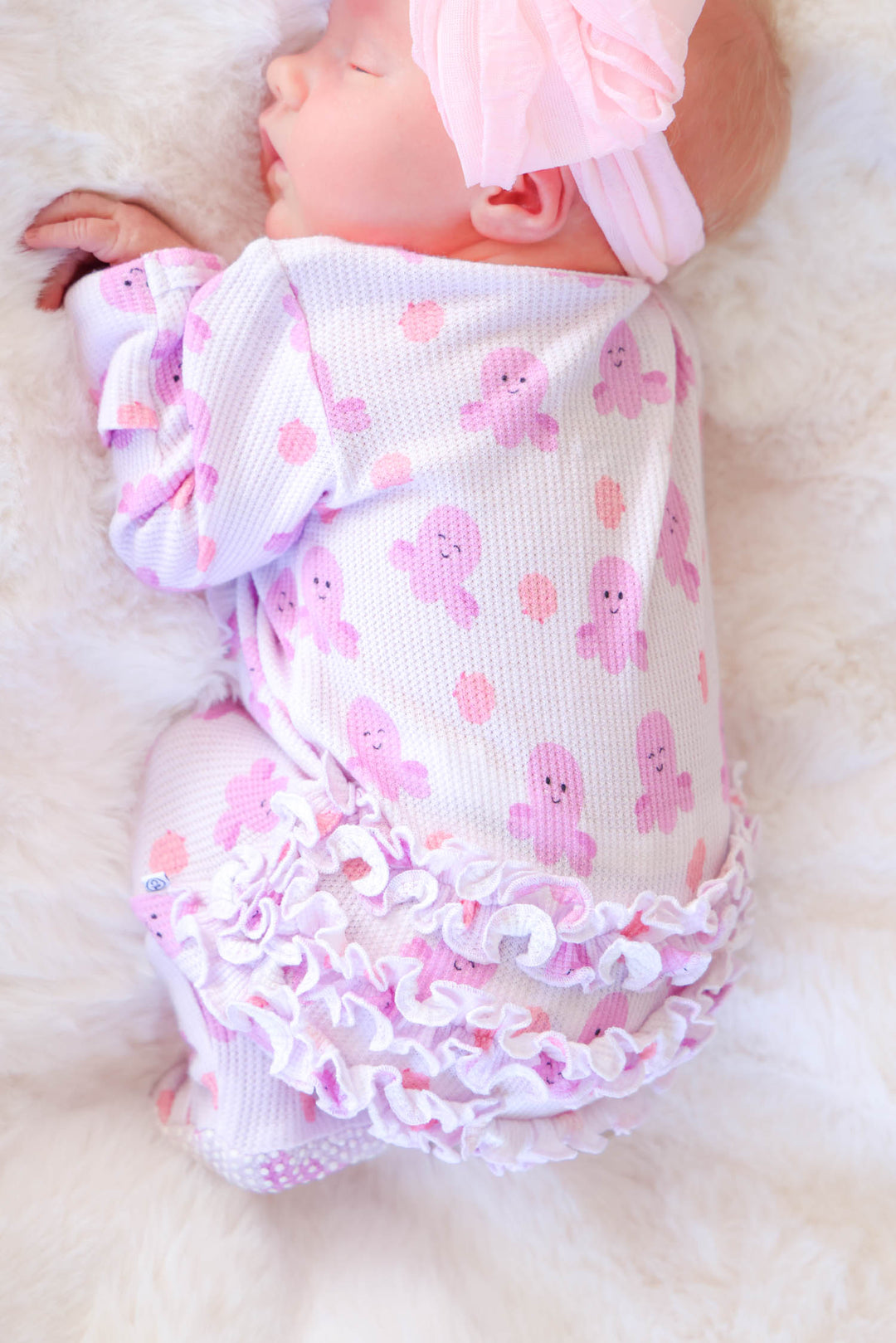 newborn wearing sea snuggles bamboo waffle ruffle zipper footie on white fur — side view highlighting ruffle bum and zipper
