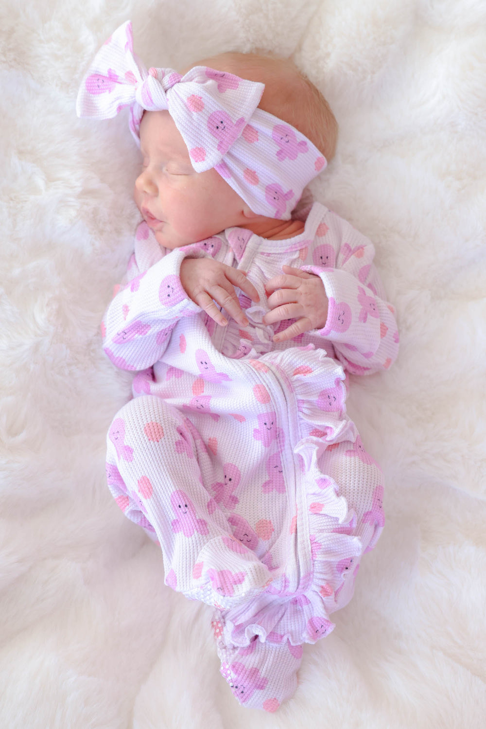 newborn in sea snuggles bamboo waffle ruffle footie wearing matching sea snuggles bamboo waffle knit large bow headwrap on white fur
