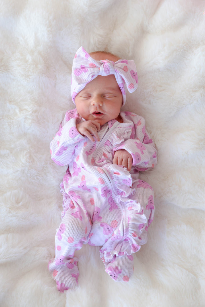newborn on white fur wearing sea snuggles bamboo waffle knit bow headwrap with matching ruffle zipper footie — overhead lifestyle view