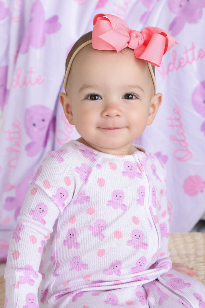 smiling baby in sea snuggles romper with coral bow headband — personalized sea snuggles octopus print kids blanket in background
