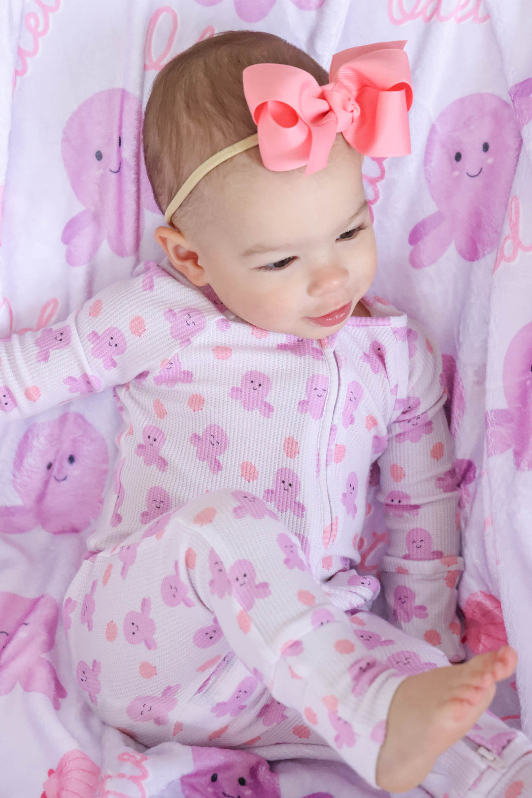 baby in sea snuggles bamboo waffle convertible zip romper resting on personalized sea snuggles kids blanket with coral bow headband