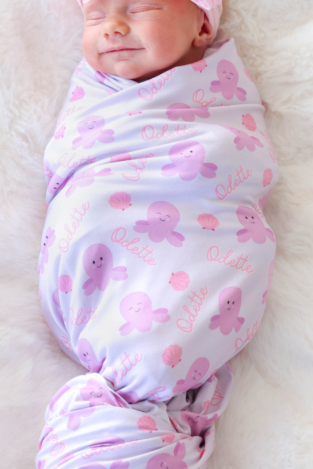 smiling newborn in personalized sea snuggles swaddle blanket with custom name wearing matching sea snuggles bamboo waffle bow headwrap