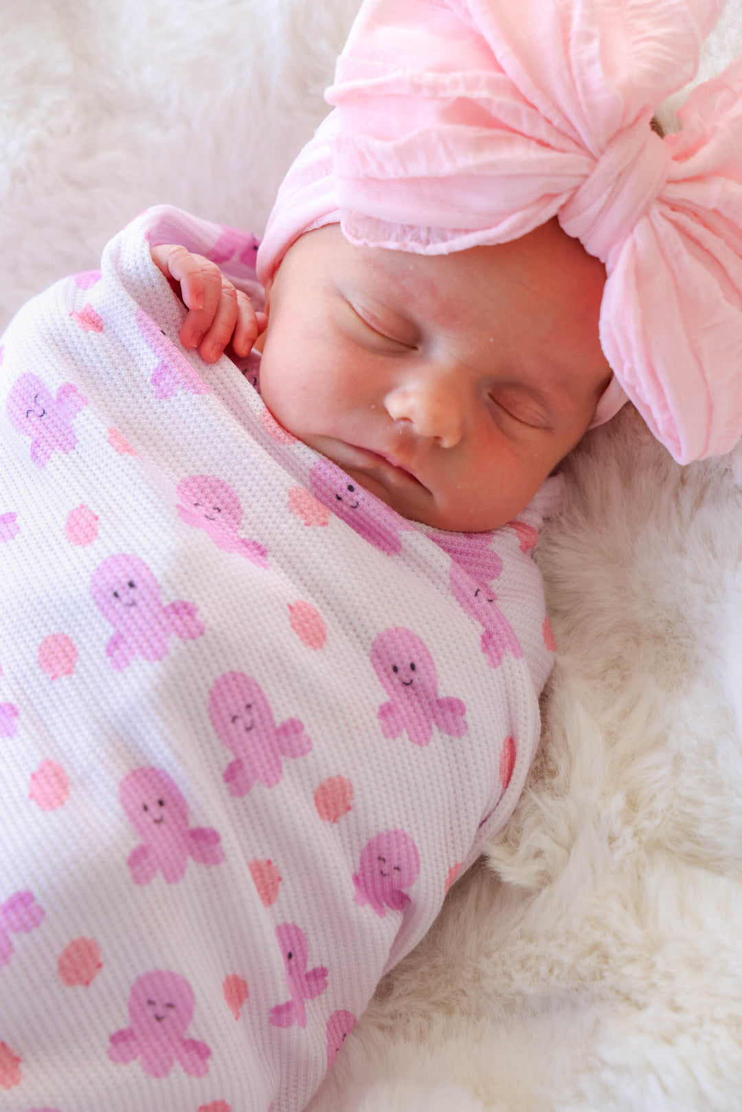close-up of sleeping newborn face swaddled in sea snuggles bamboo waffle oversized swaddle blanket with large pink tulle bow headband