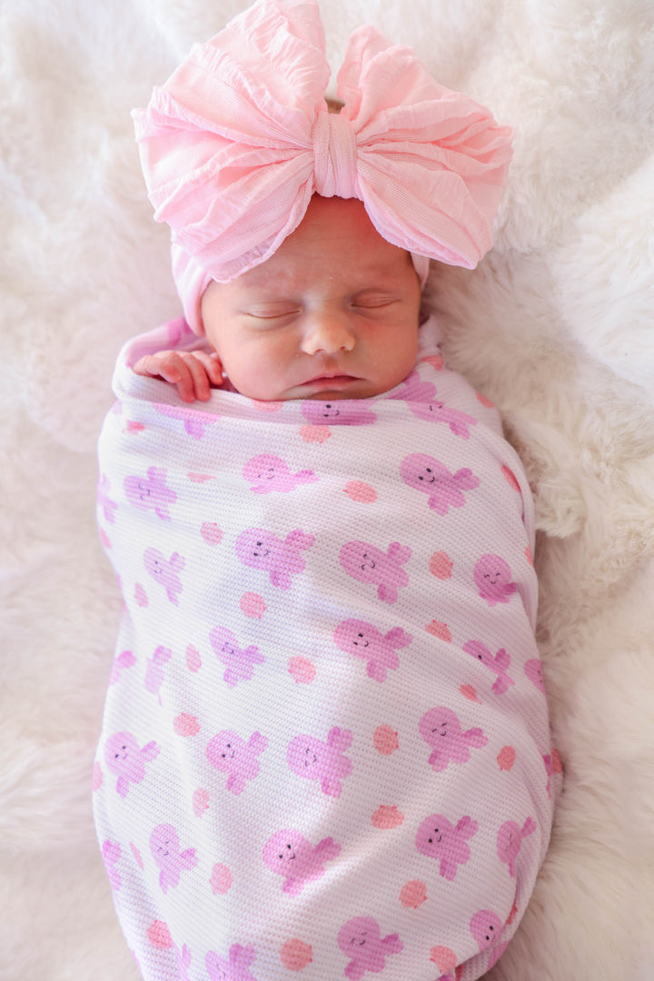 newborn swaddled in sea snuggles bamboo waffle oversized swaddle blanket on white fur with large pink bow headband
