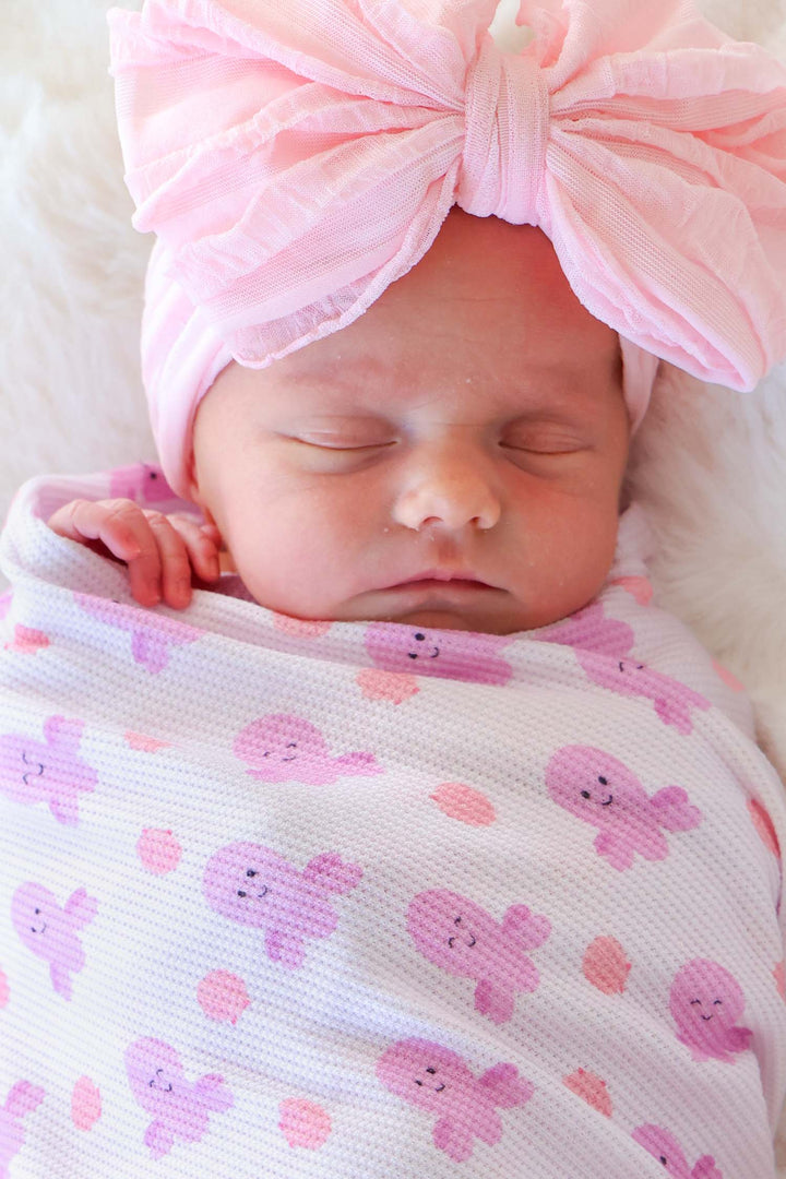 sleeping newborn swaddled in sea snuggles bamboo waffle oversized swaddle blanket with large pink tulle bow headband — close-up portrait