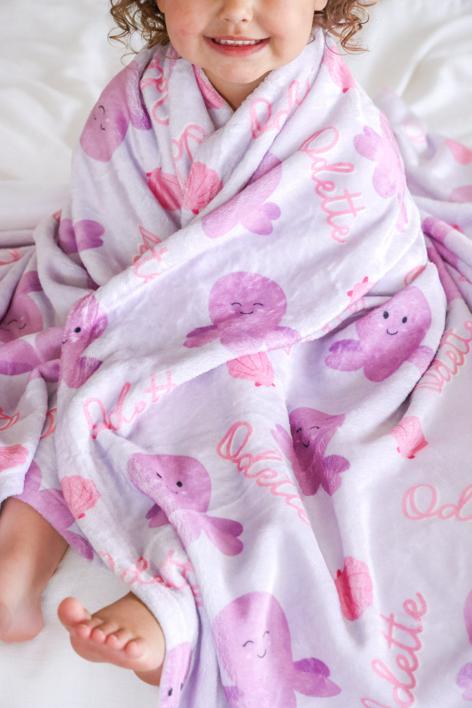 personalized sea snuggles kids blanket folded on white background — showing octopus and seashell print with custom name in pink script