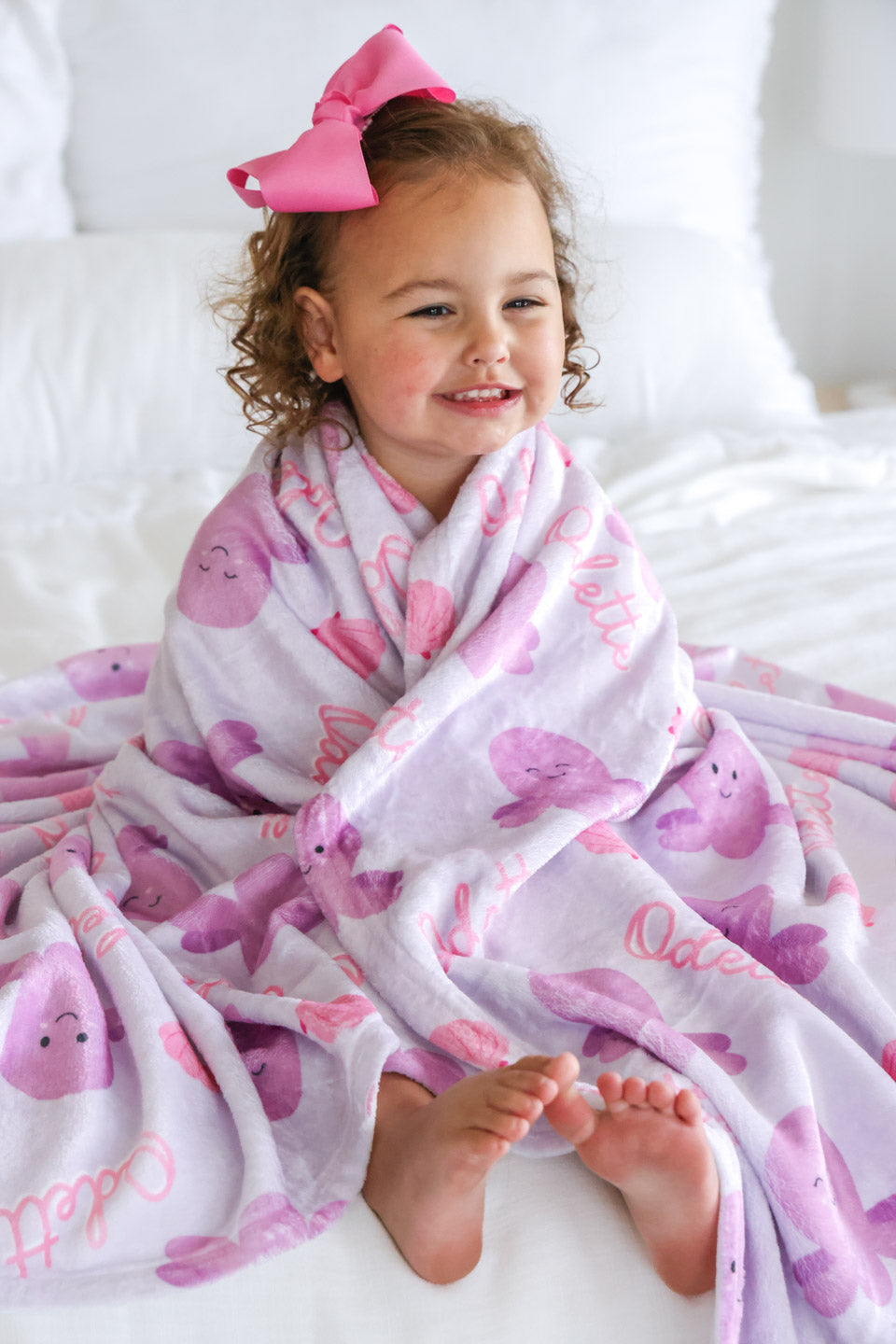 toddler on white bedding wrapped in personalized sea snuggles kids blanket with lavender octopus print and custom name — full body lifestyle