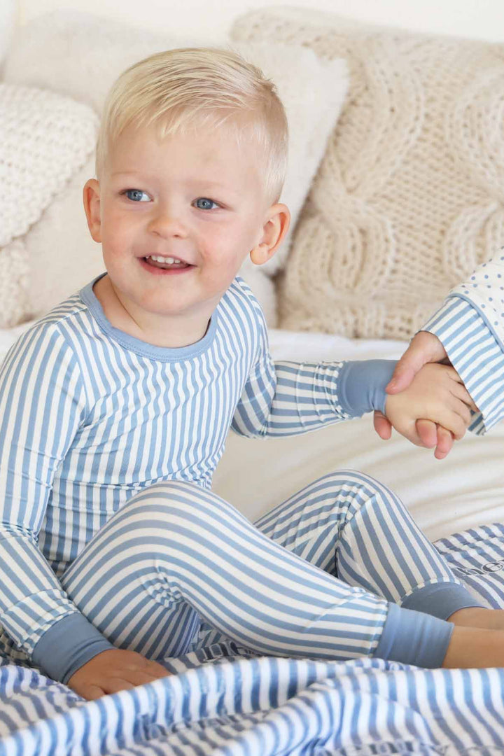 boy wearing a blue and white stripe long sleeve pajama set with mom holding his hand in coordinating polka dot lounge set with stripe detailing on sleeves