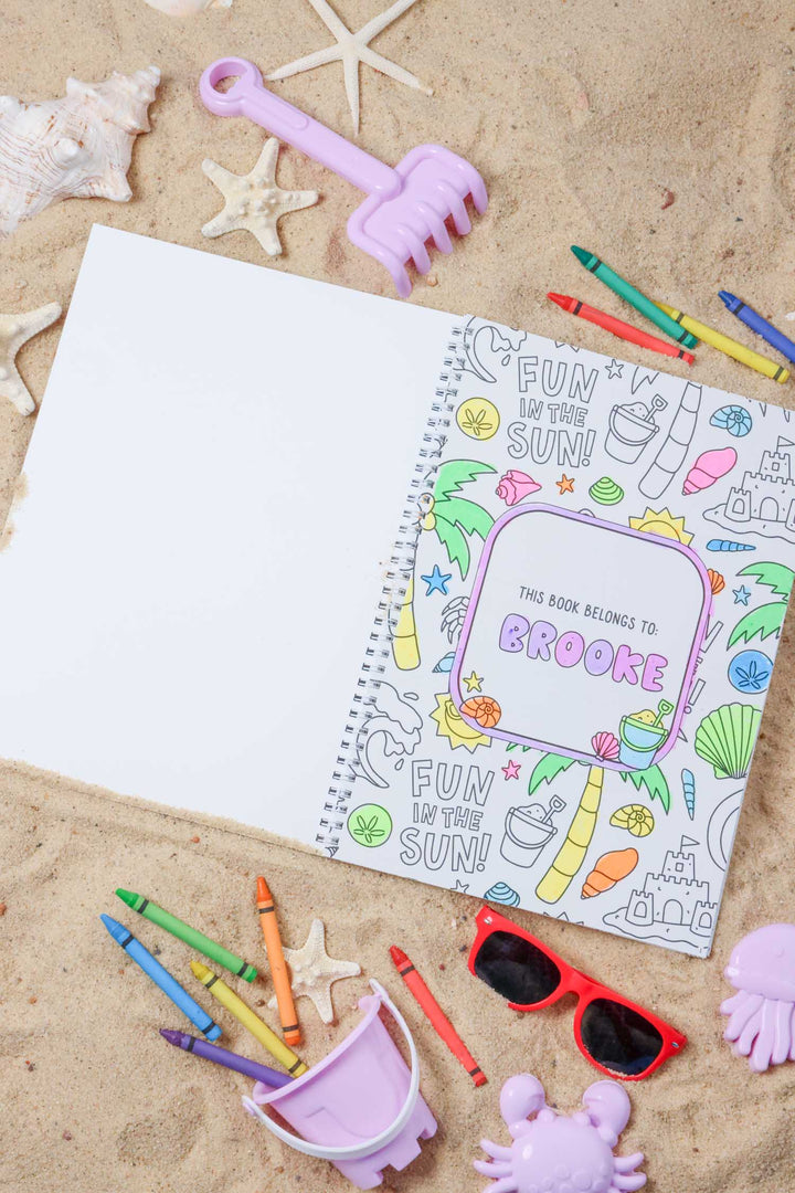 Personalized cover page reading 'This book belongs to: Brooke' with 'Fun in the Sun' beach doodles, partially colored, resting on sand with sunglasses and beach toys.