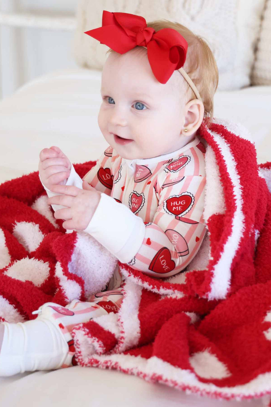 baby girl sitting on a bed in a pink and white stripe pajama romper with pink and red conversation heart candy for valentine's day 