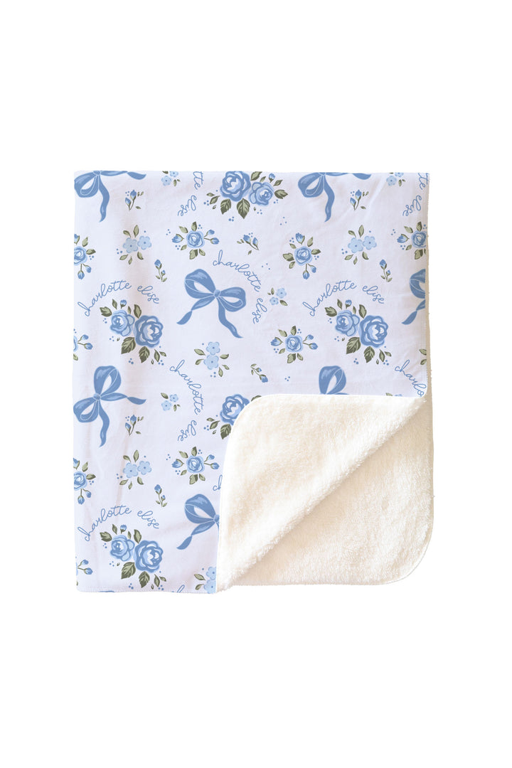 Folded Tied In Blooms blanket showing the blue floral and bow print on one side and soft sherpa fleece lining on the reverse