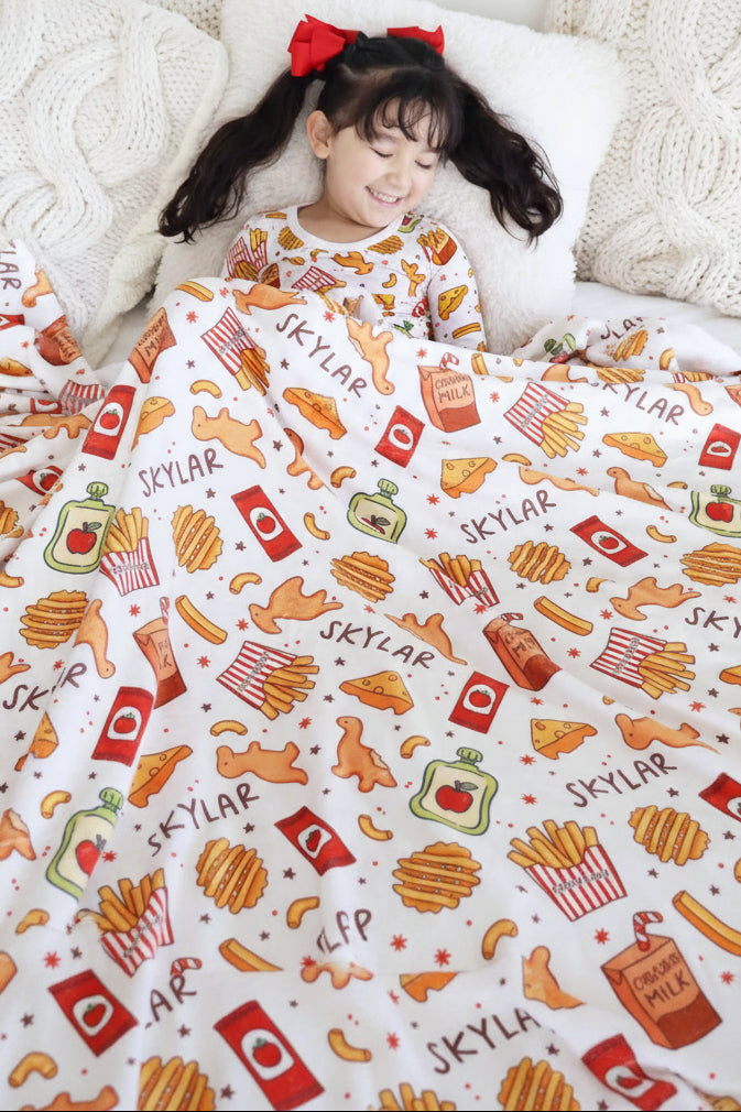 girl laying on bed in snack themed pajama set with a matching personalized blanket over her 