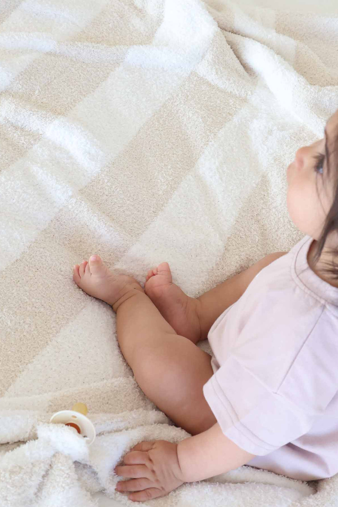 baby girl sitting on a beige and white stripe microfiber blanket next to a matching lovey