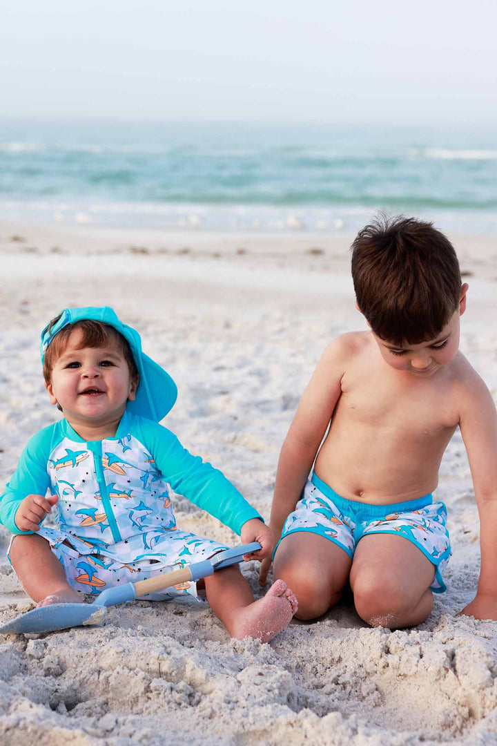 two boys playing in the sand wearing coordinating surfing shark swimsuits 
