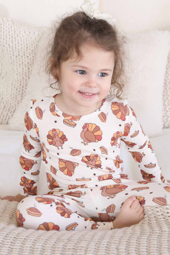 girl sitting on bed wearing Caden Lane thanksgiving two piece pajama set 