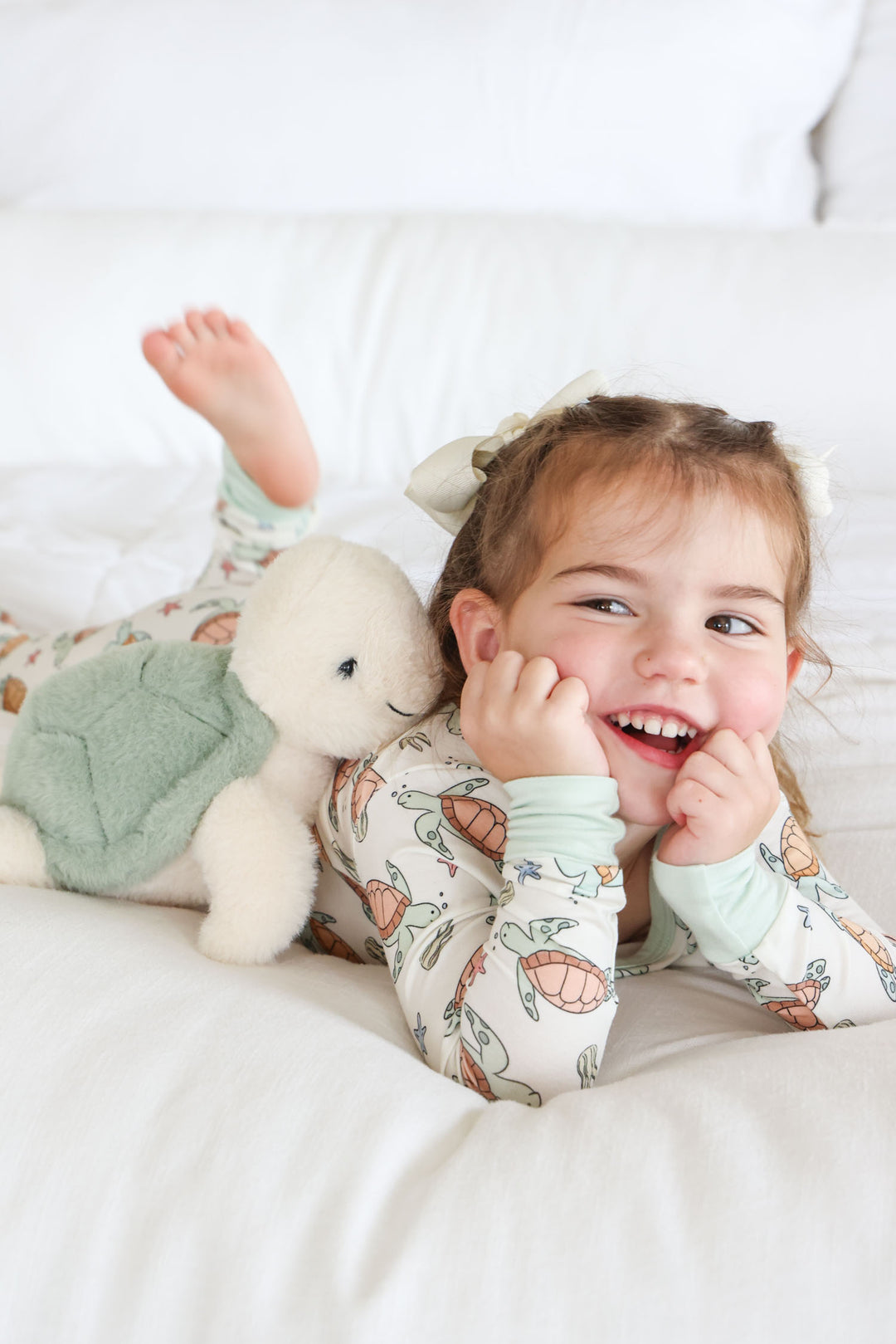 girl laying on stomach in turtle pajamas with a stuffed turtle next to her 