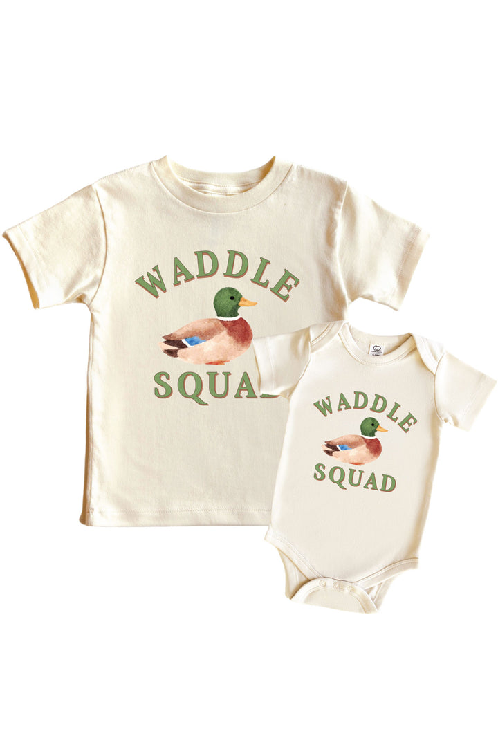 Natural Waddle Squad graphic kids tee and baby bodysuit displayed together, each with WADDLE SQUAD text and mallard duck illustration on front