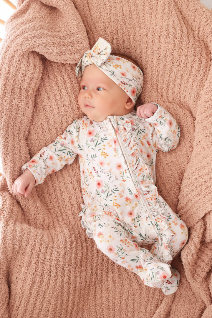 baby wearing one piece zip footie in girly florals and light pink accents with matching newborn bow headwrap