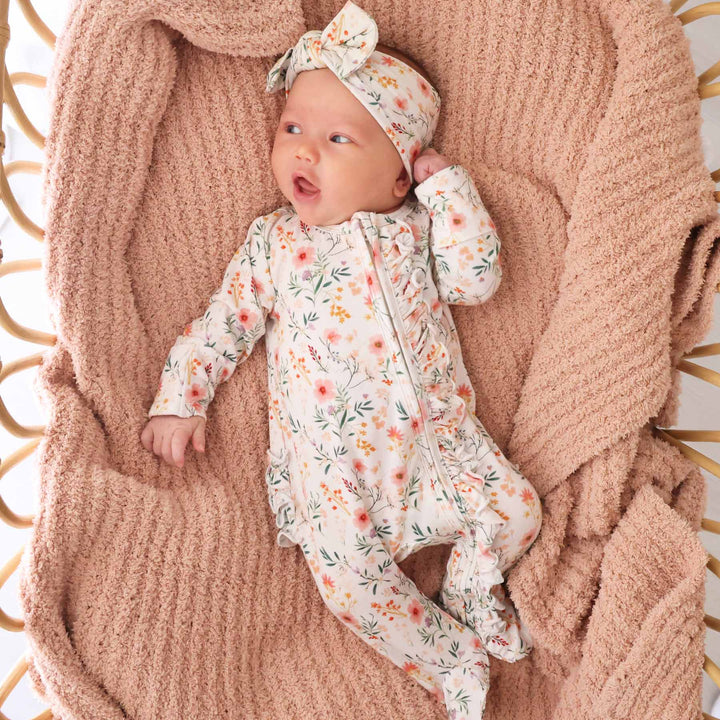 baby wearing zip footie romper in girly wildflower print with ruffles with matching newborn bow headwrap