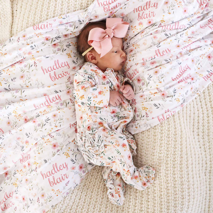 baby wearing ruffle butt zip footie romper in dainty floral print with matching personalized printed blanket