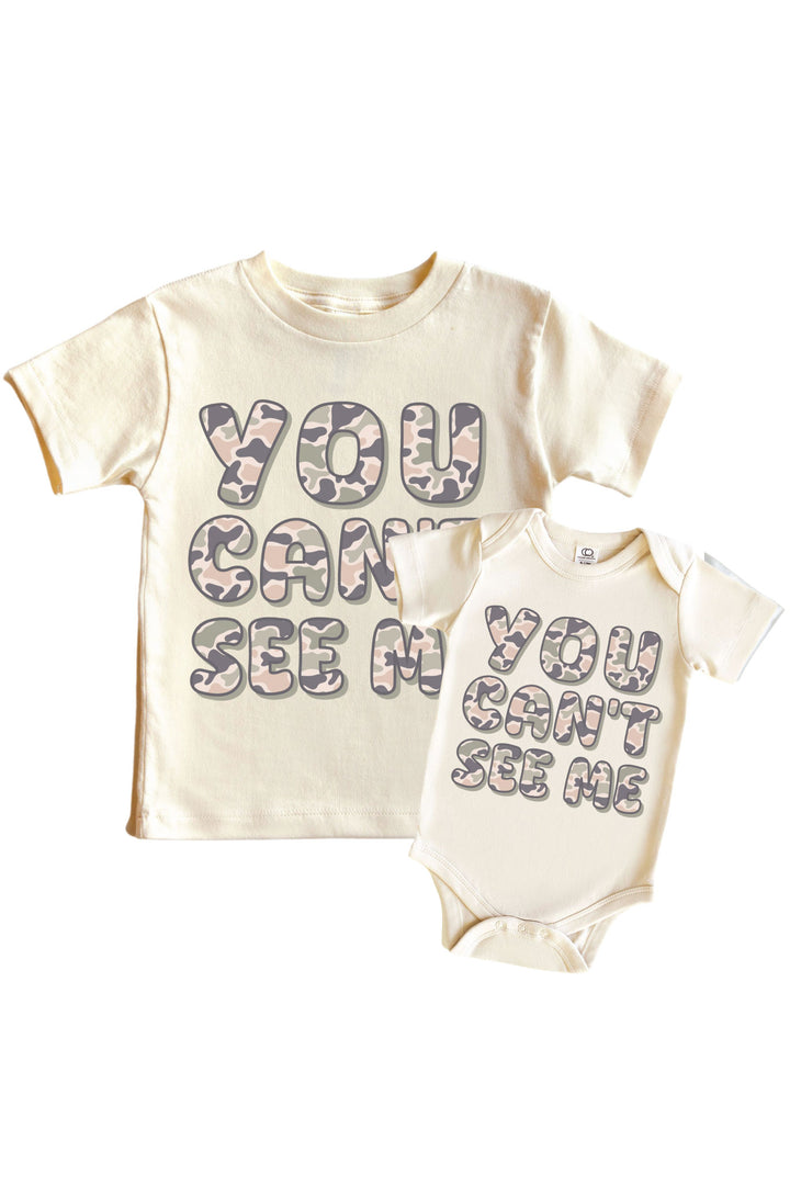 Natural cream kids graphic tee and baby bodysuit with "You Can't See Me" camo print slogan side by side